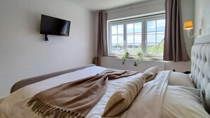 A hotel room with a bed, a TV mounted on the wall, a window with curtains, and a plant on the windowsill. - 5 bedroom beautiful home in Westende (Westende)