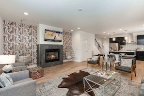 A modern living room with a fireplace, a flat-screen TV, a dining area, and a kitchen.