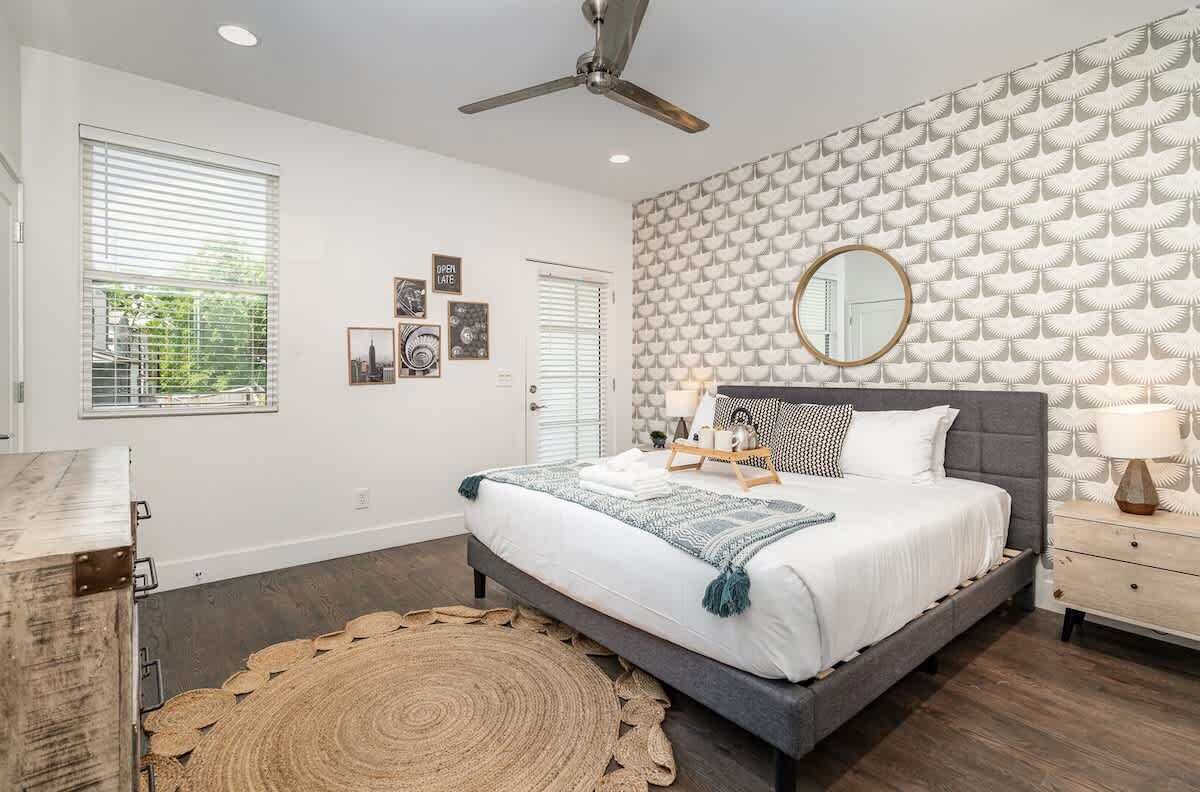 A bedroom with a bed, a ceiling fan, a patterned wall, and a window with blinds.