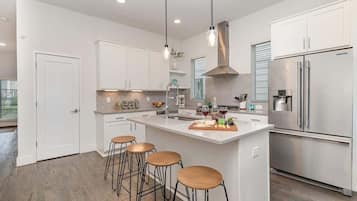 A modern kitchen with white cabinets, a stainless steel refrigerator, and a central island with stools.