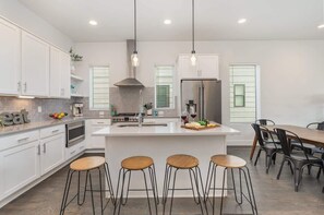 A modern kitchen with white cabinetry, a central island with stools, a stainless steel refrigerator, and pendant lighting.