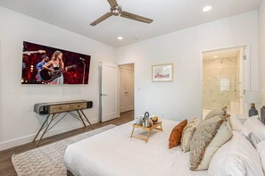 A bedroom with a bed, a TV, a ceiling fan, a door, and a bathroom visible through an open door.