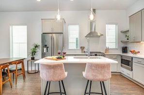 A modern kitchen with a central island, pendant lights, and a dining area with wooden chairs. - Limbo-East Nashville-Mins to Germantown & Broadway (Nashville)