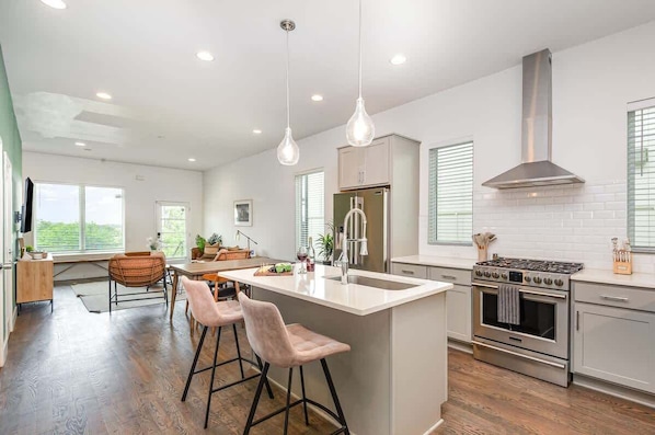 A modern kitchen with a central island, stainless steel appliances, pendant lighting, and a view of the outdoors.