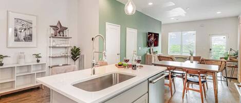 A modern kitchen with a white island, stainless steel sink, and pendant lighting.