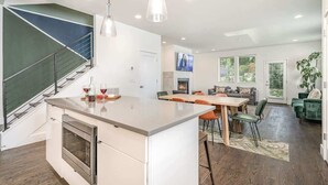 A modern kitchen with a built-in oven, a dining area with a wooden table and chairs, and a staircase with a green accent wall.