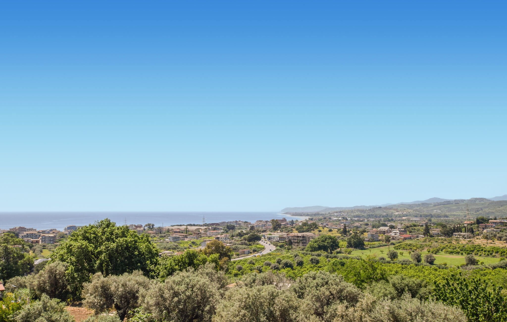 A coastal town with a clear view of the sea, surrounded by greenery and residential buildings.