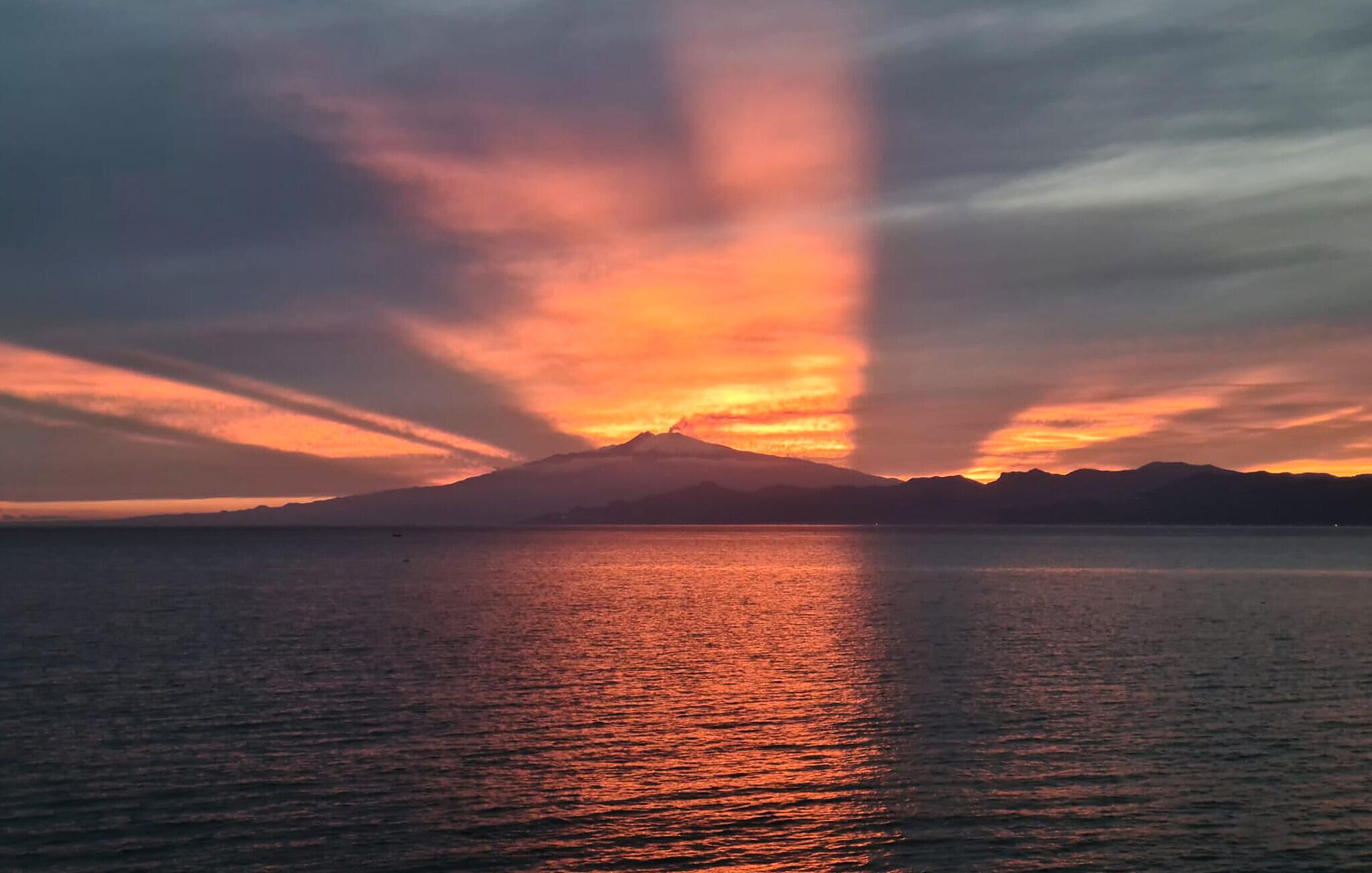 Un atardecer sobre una superficie acuática tranquila con la silueta de una montaña al fondo.