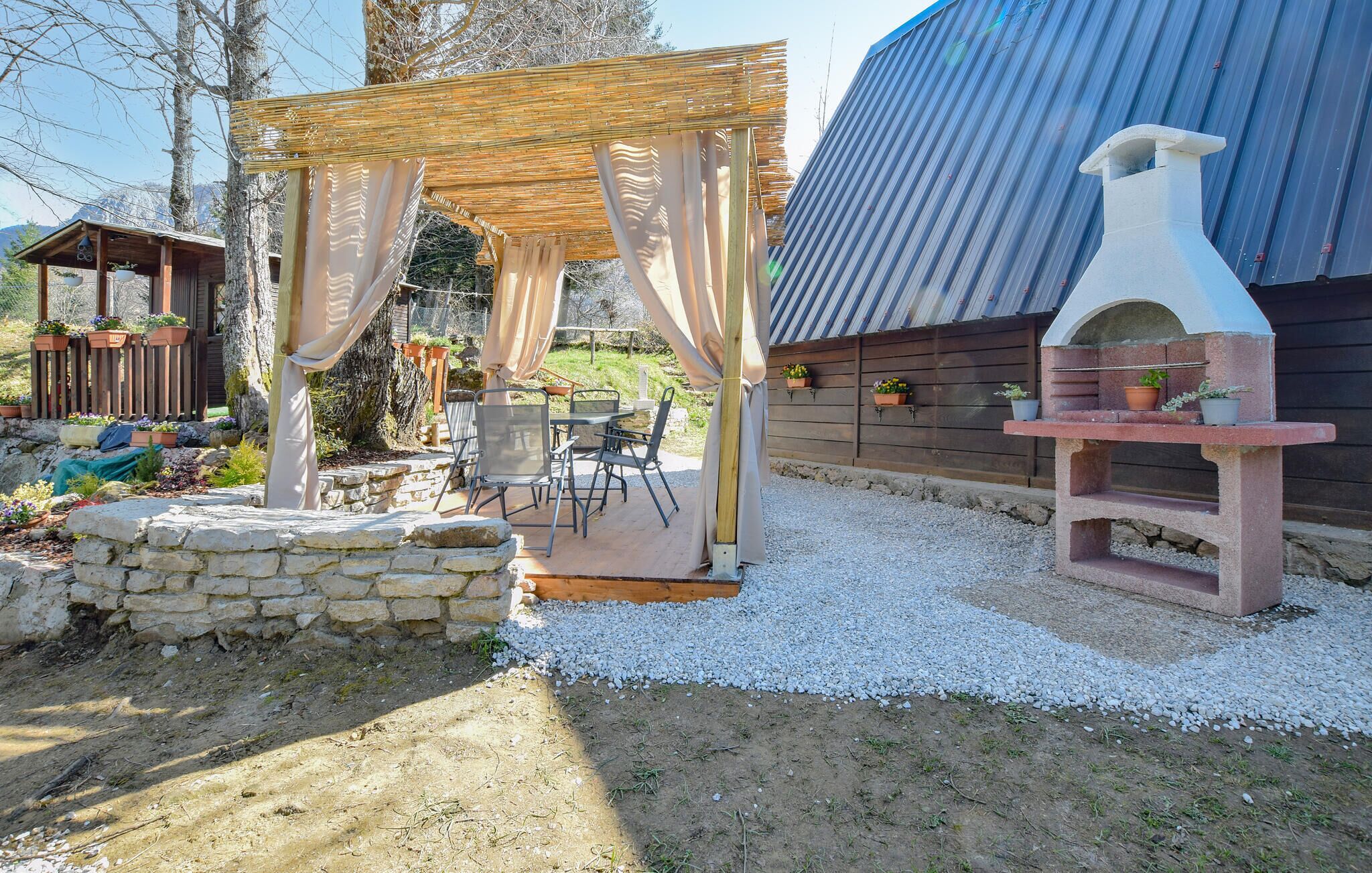 Een terras met een pergola, zitplaatsen buiten en een pizzaoven.