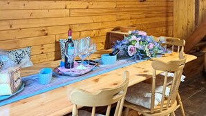 Une table de salle à manger en bois, accompagnée de chaises, une bouteille de vin, des verres, un bol bleu et un arrangement floral.