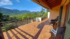 Una terraza con vistas a montañas, una mesa con sillas y una parrilla.