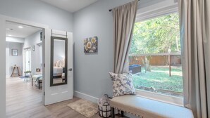 Una habitación con un banco junto a una ventana, una puerta que da a otra estancia y una pequeña mesa con una silla.