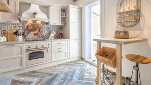 A modern kitchen with white cabinetry, a herringbone-patterned floor, a vintage-style coffee machine, and a rustic wooden table with a metal stool. - Le Rêve by Interhome (Valledoria)
