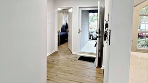 Een gang met houten vloer die leidt naar een kamer met een bed en gordijnen.