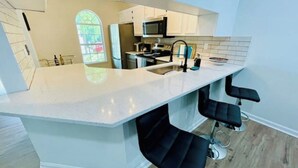 Een moderne keuken met een centraal eiland, barkrukken en een groot raam.