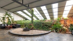 Un vaste espace intérieur doté d’un sol en pierre, d’un espace salon circulaire et d’une variété de plantes et de verdure.