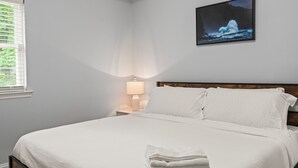 A neatly made bed with white linens, a bedside lamp, and a framed picture of an iceberg on the wall.