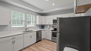 A modern kitchen with white cabinets, a stainless steel refrigerator, and a wooden floor.