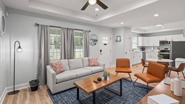 A modern living room with a grey sofa, orange chairs, a wooden coffee table, and a ceiling fan.