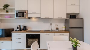 Una cocina moderna con armarios blancos, un refrigerador de acero inoxidable, un microondas y una cafetera.