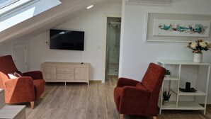Un salón moderno con dos sillones rojos, un aparador de madera, un televisor montado en la pared y un cuadro sobre un estante blanco con una planta.