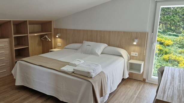 Un dormitorio con una cama grande, un armario de madera y vistas a zonas verdes por una ventana.