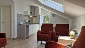 Una cocina moderna con microondas, tostadora y cafetera. Hay dos sillas rojas y una mesa con un jarrón de flores. Un reloj está en la pared.