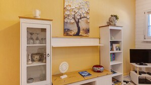 A room with a cabinet, a painting, a shelf with books, a television, and a decorative item. - Holiday Apartment 'Fleur' with Wi-Fi (Tengen)