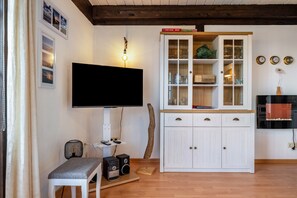 Una sala de estar con un televisor de pantalla plana, un armario blanco, un banco y suelo de madera.