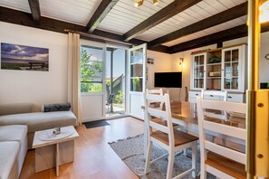 Una sala moderna con un sofá, una mesa de comedor y sillas. Hay un televisor montado en la pared y una ventana con cortinas.