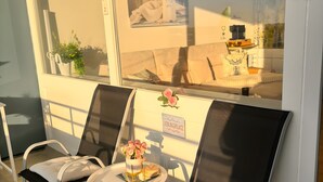 A balcony with two chairs, a small table, and a vase with flowers.