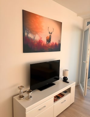 Ein modernes Wohnzimmer mit einem Flachbildfernseher, einer weißen Unterhaltungseinheit und einem gerahmten Bild von einem Hirsch.