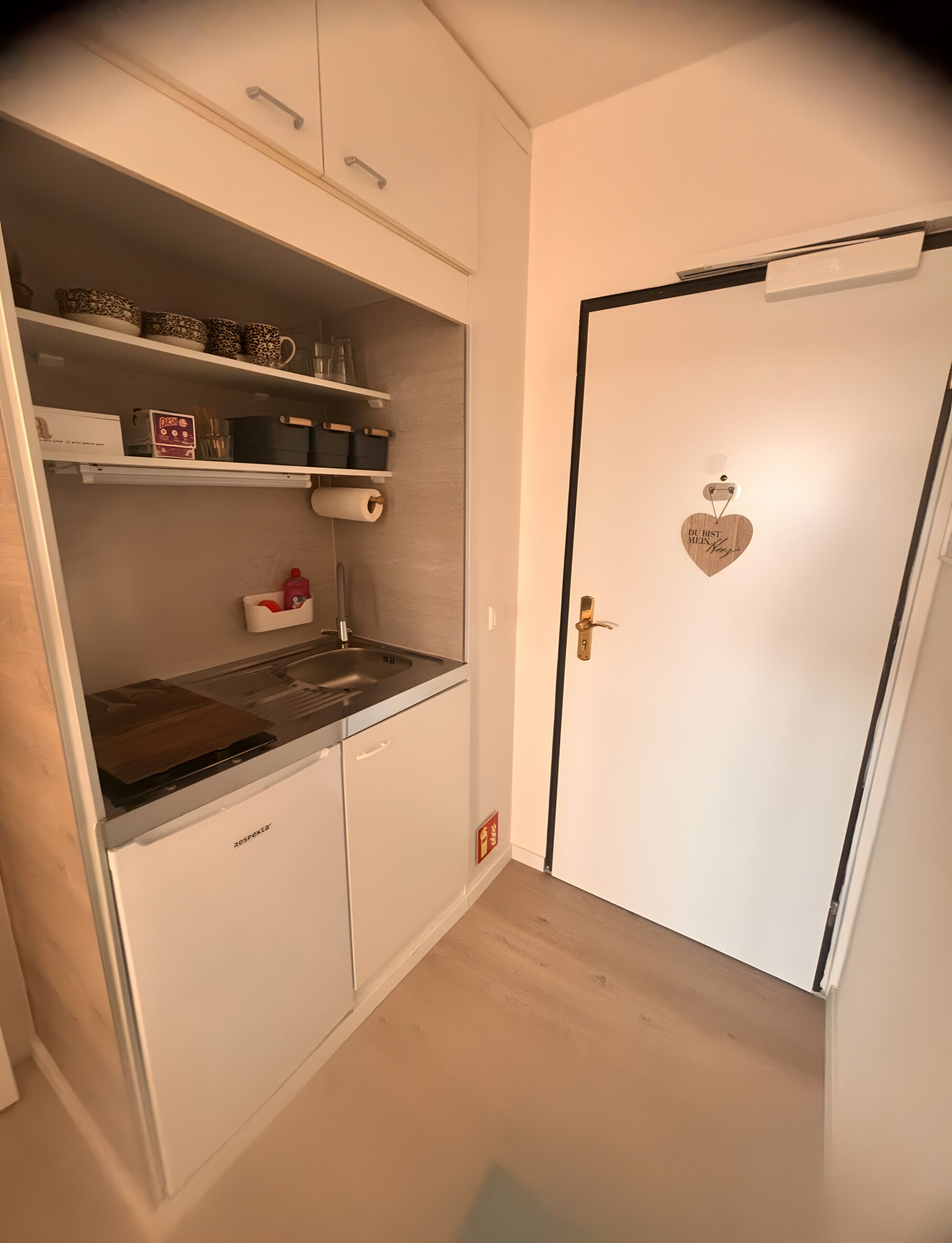 Una cocina con armarios blancos, un fregadero y una puerta con un adorno en forma de corazón.