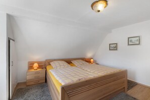 A bedroom with a wooden bed, two bedside tables with lamps, a door, and two framed pictures on the wall.