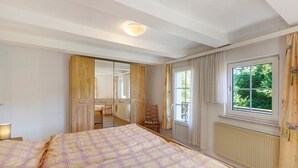 Een slaapkamer met een bed, een raam met gordijnen, een radiator en een spiegel.