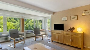 Een moderne woonkamer met een televisie, een houten kast en twee stoelen.