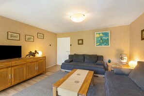 A living room with a sofa, a coffee table, a TV, and framed pictures on the wall. - Apartment 'Demberg' with Mountain View, Private Terrace and Wi-Fi (Schmallenberg)