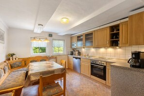 A kitchen with wooden cabinets, a dining table, chairs, a built-in oven, and a coffee maker. - Apartment 'Demberg' with Mountain View, Private Terrace and Wi-Fi (Schmallenberg)
