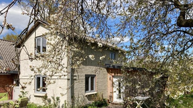A two-story house with a brick facade, a small front porch, and a garden area with a wooden bench.