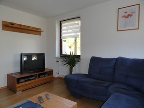 A living room with a TV, sofa, coffee table, and a window with blinds.