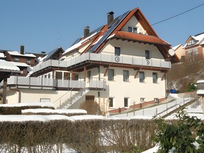 A multi-story building with a sloped roof, balconies, and a staircase leading to the upper floors.