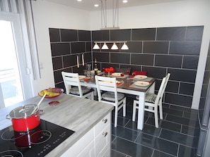 A modern kitchen with a dining area, black and white tiled walls, a red pot on the stove, and a table set for two. - Am Keschtewäldele – Holiday Apartment in the Northern Black Forest (Forbach)