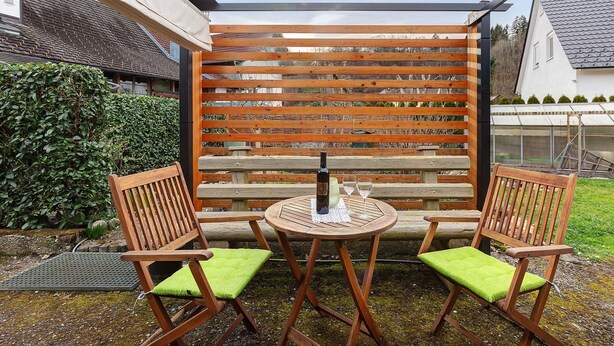 Un espace extérieur aménagé avec des meubles en bois, comprenant une table et des chaises, une bouteille et deux verres.