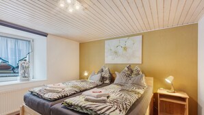 Un lit double avec une literie à motifs, une table de chevet avec une lampe, une fenêtre donnant sur une voiture et une œuvre d’art accrochée au mur.