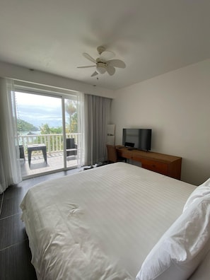 Habitación de hotel con una cama grande, un escritorio con silla, televisor y balcón con vista al mar.