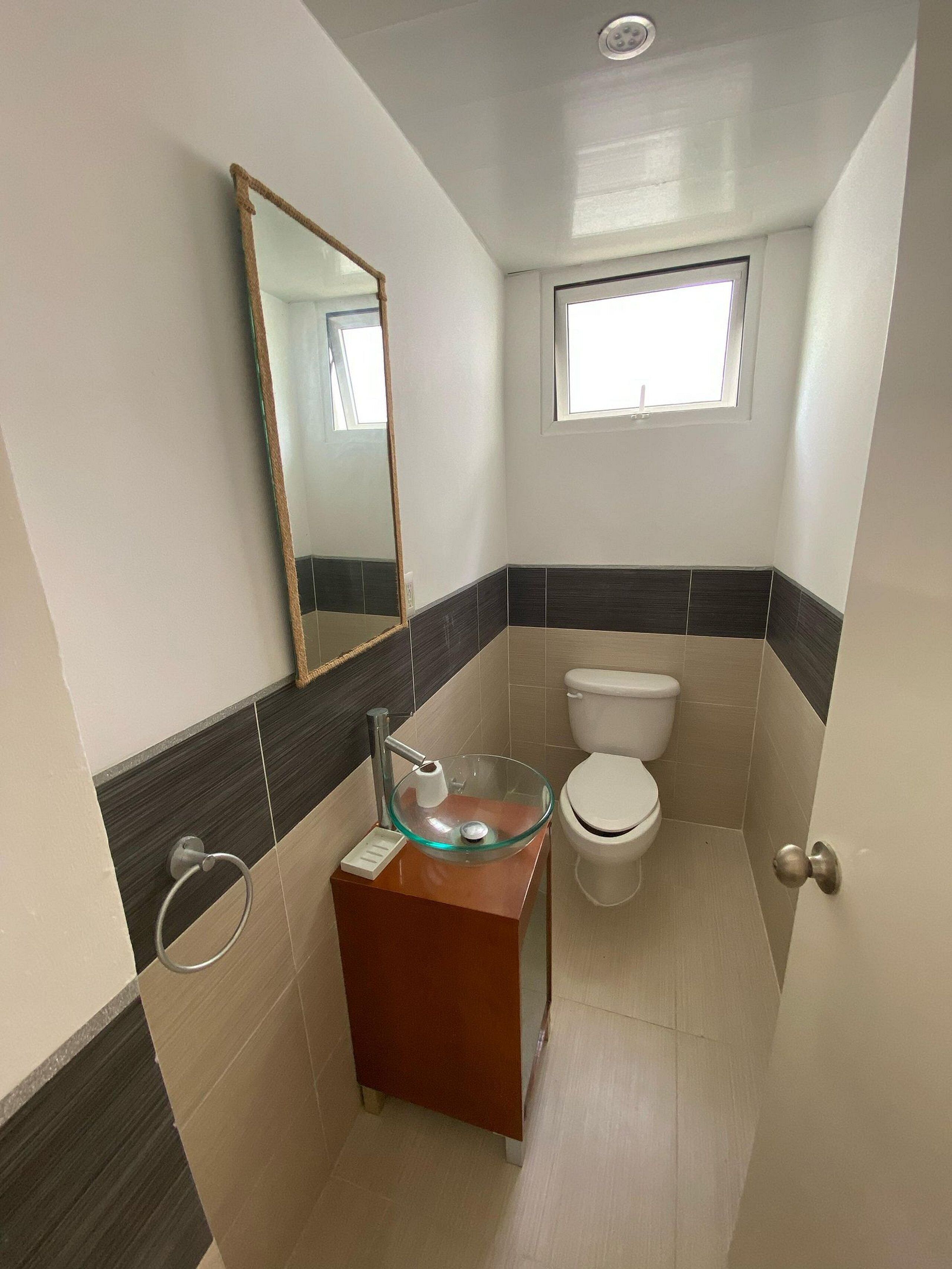 A bathroom with a glass bowl sink, a toilet, and a mirror.