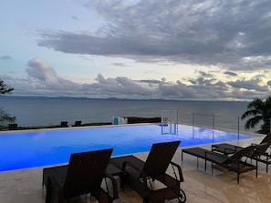 Una piscina infinita con sillones de descanso, vista al mar y cielo nublado.