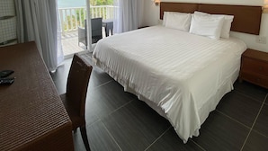 A hotel room with a large bed, a desk with a chair, a ceiling fan, and a balcony with a view.
