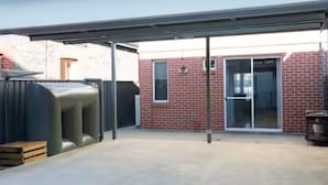Un espace extérieur abrité, avec un bâtiment en briques, une porte-fenêtre coulissante et un barbecue.