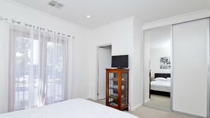 Une chambre à coucher comprenant un lit, un téléviseur posé sur un meuble en bois, une armoire et une porte coulissante donnant sur une autre pièce.
